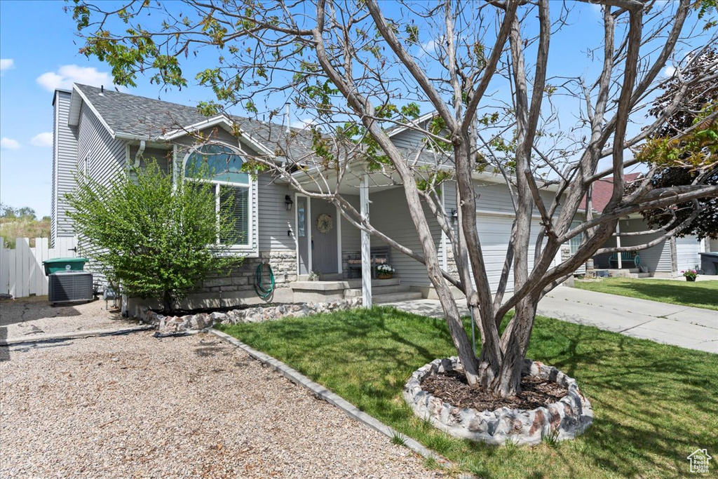 View of property hidden behind natural elements with driveway, central air condition unit, and an attached garage