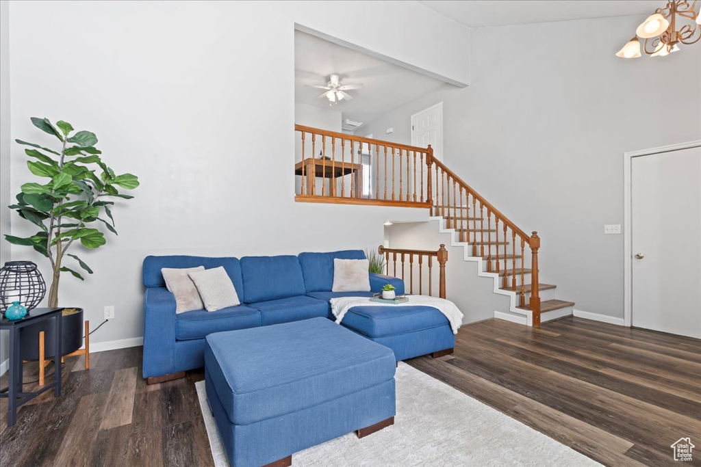 Living room featuring wood finished floors, a ceiling fan, stairs, baseboards, and a high ceiling