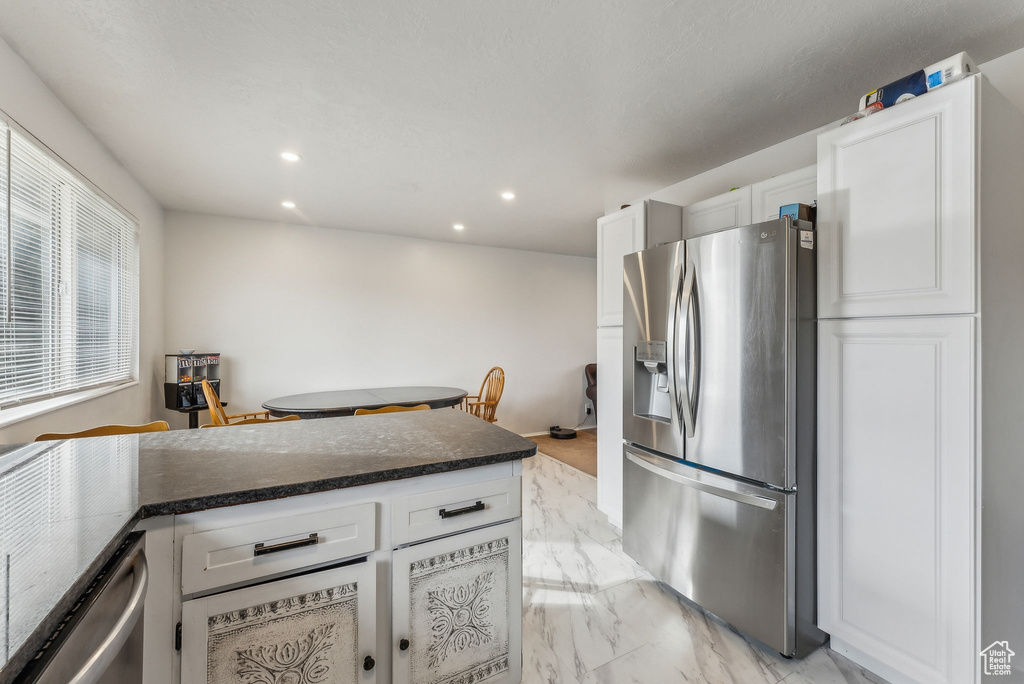 Kitchen with stainless steel fridge, dark countertops, recessed lighting, white cabinets, and light marble finish flooring