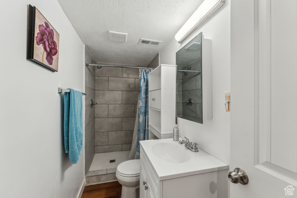 Bathroom with a textured ceiling, vanity, a stall shower, wood finished floors, and toilet