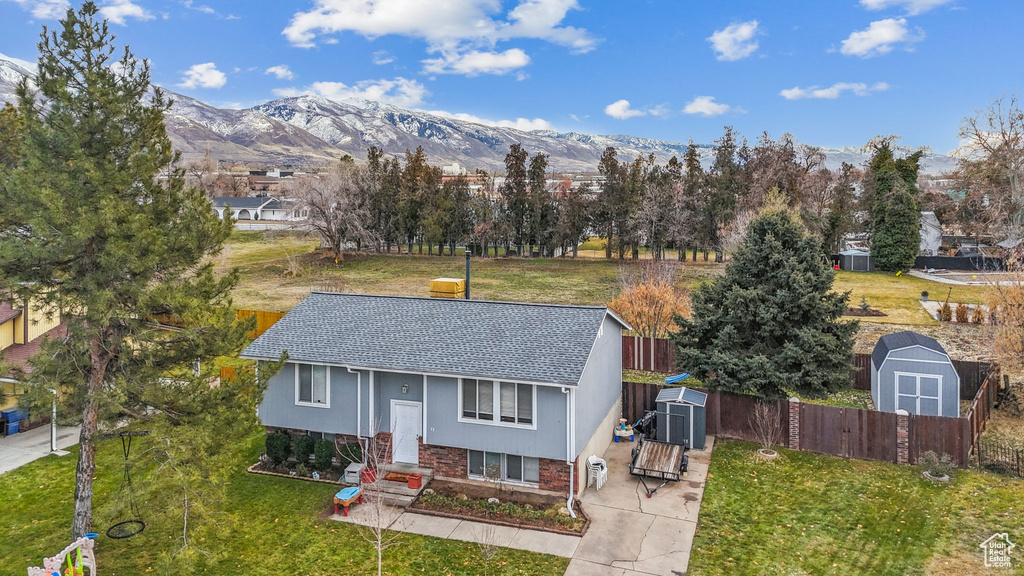 Bi-level home with a shed, an outbuilding, a shingled roof, and a mountain view