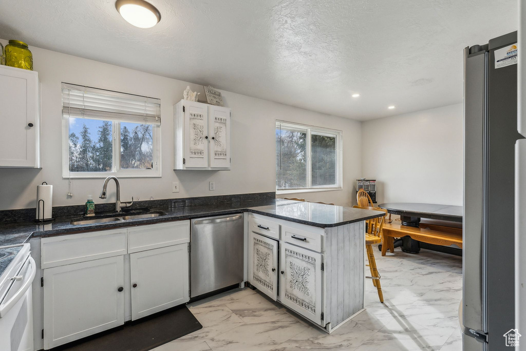 Kitchen with stainless steel appliances, a sink, light marble finish flooring, a peninsula, and white cabinetry