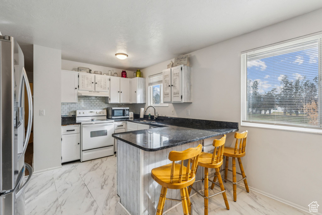 Kitchen featuring stainless steel appliances, a peninsula, a sink, light marble finish flooring, and white cabinetry