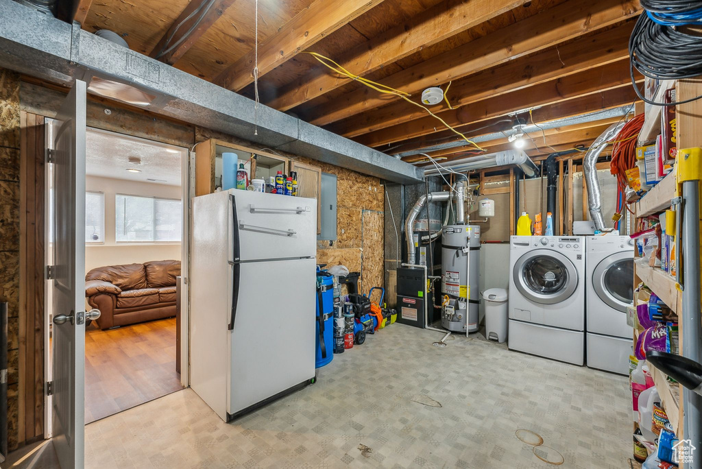 Basement with freestanding refrigerator, strapped water heater, electric panel, and washing machine and dryer