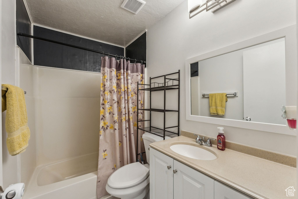 Full bath featuring toilet, vanity, shower / bath combo, and a textured ceiling