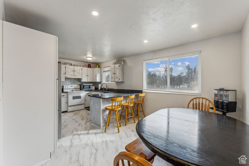 Kitchen featuring white range with electric cooktop, light marble finish flooring, stainless steel microwave, a peninsula, and recessed lighting