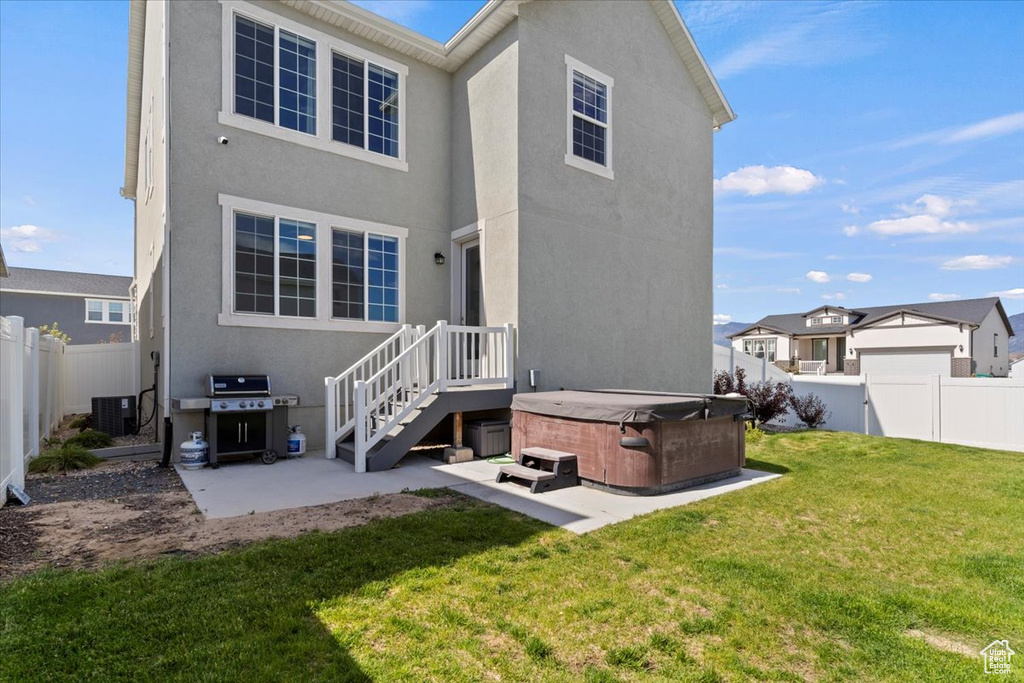 Rear view of property with a hot tub, a patio, stucco siding, and central AC