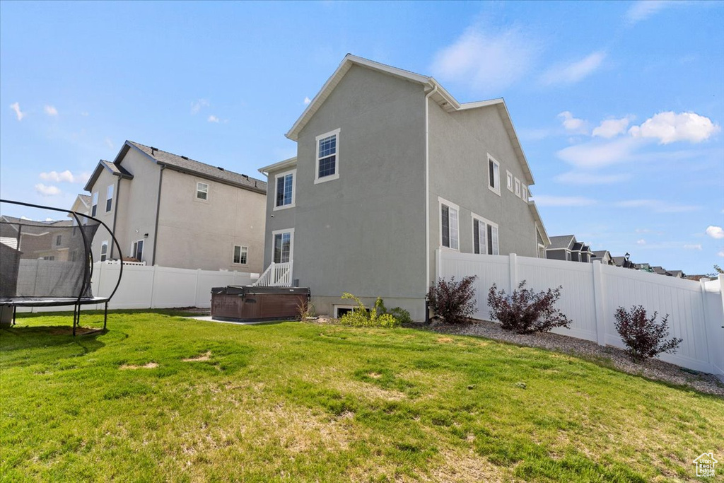 Rear view of property with a hot tub, a trampoline, and stucco siding