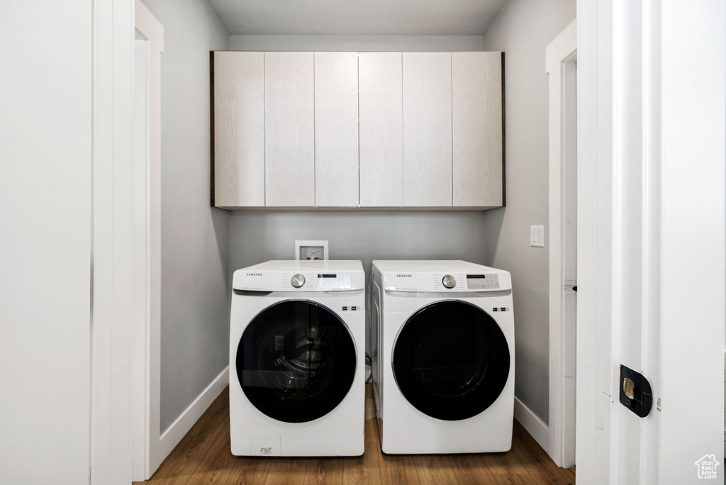 Laundry area featuring cabinet space, washer and dryer, baseboards, and wood finished floors