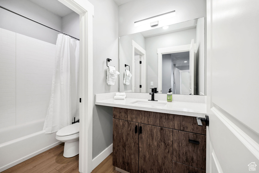 Full bath with wood finished floors, toilet, vanity, shower / tub combo with curtain, and baseboards