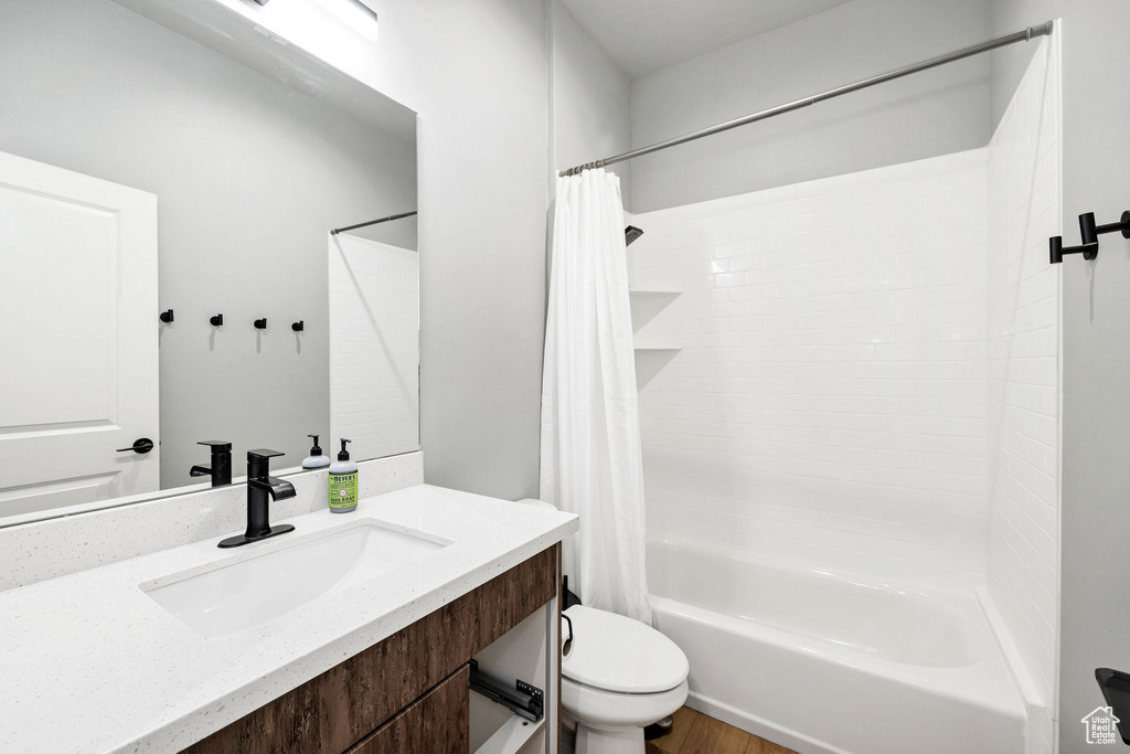 Bathroom with toilet, shower / bathtub combination with curtain, vanity, and wood finished floors