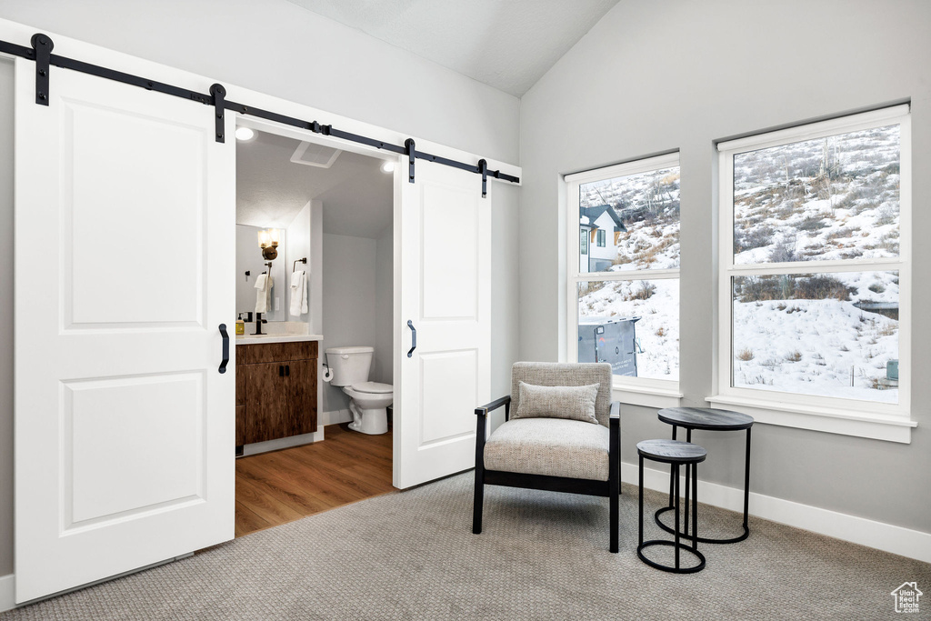 Sitting room with a barn door, vaulted ceiling, carpet floors, and baseboards