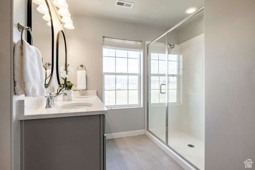 Bathroom featuring healthy amount of natural light, double vanity, a shower stall, and tile patterned flooring