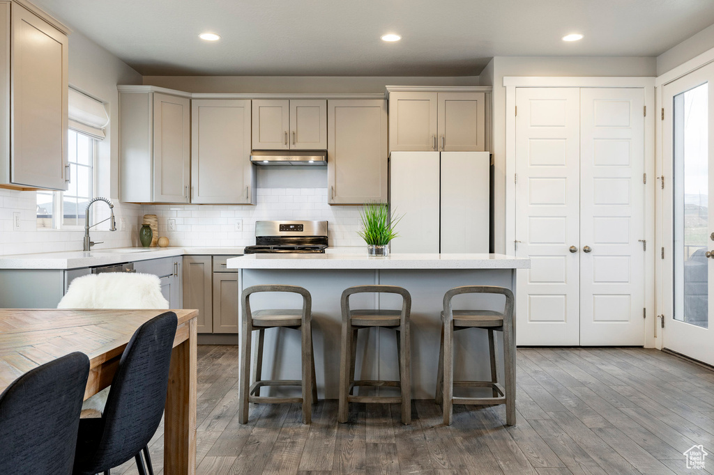 Kitchen with freestanding refrigerator, under cabinet range hood, gas stove, a center island, and light countertops