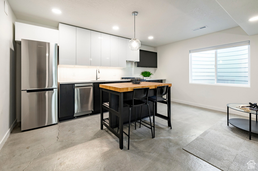 Kitchen featuring stainless steel appliances, butcher block counters, concrete floors, baseboards, and a sink