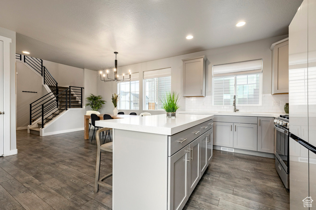 Kitchen featuring gray cabinetry, a kitchen breakfast bar, a chandelier, stainless steel gas stove, and light countertops
