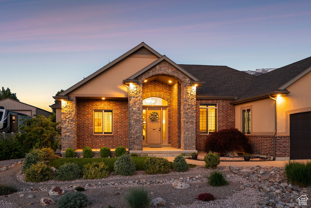 Traditional-style home with brick siding, an attached garage, roof with shingles, driveway, and stucco siding
