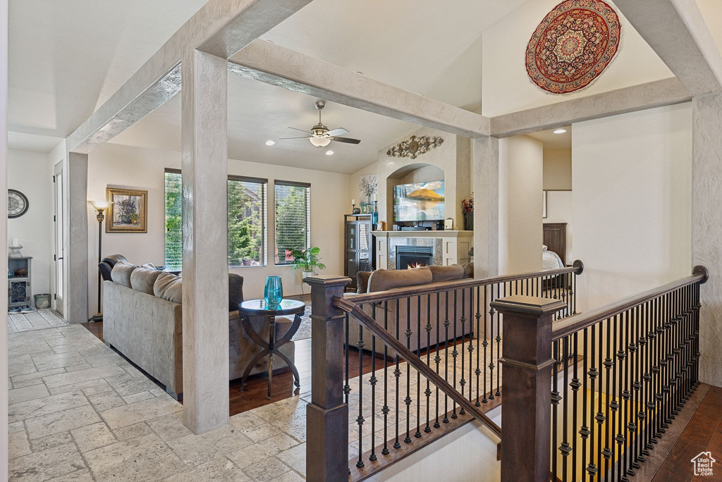 Living room featuring ceiling fan, a warm lit fireplace, stone tile flooring, recessed lighting, and vaulted ceiling