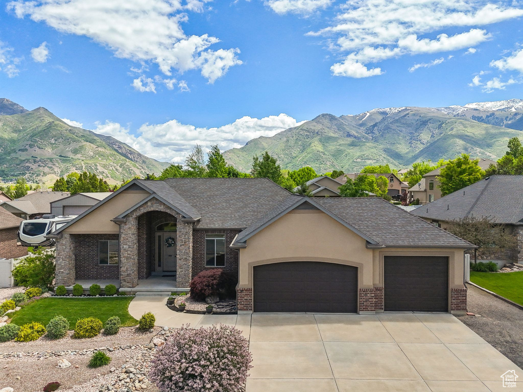 View of front of home with an attached garage, brick siding, concrete driveway, a mountain view, and stucco siding