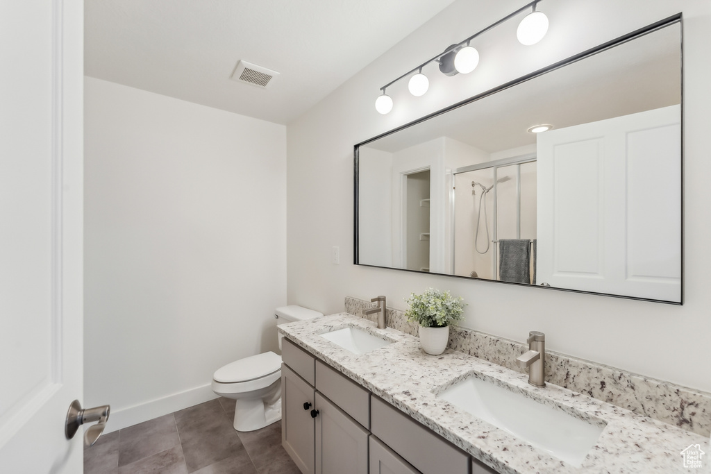 Bathroom featuring toilet, a shower stall, double vanity, baseboards, and tile patterned floors