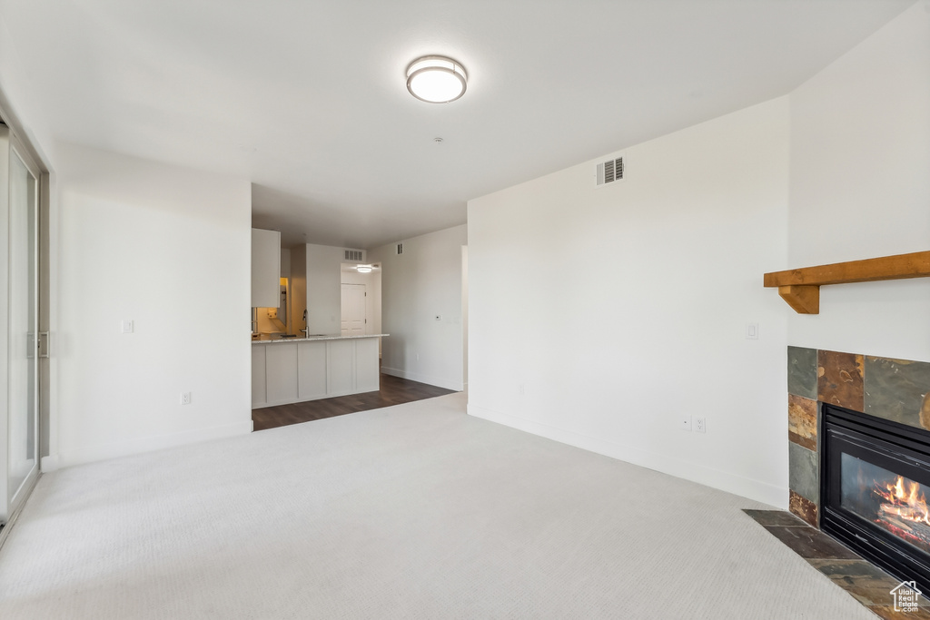 Unfurnished living room featuring dark colored carpet, a tile fireplace, and baseboards