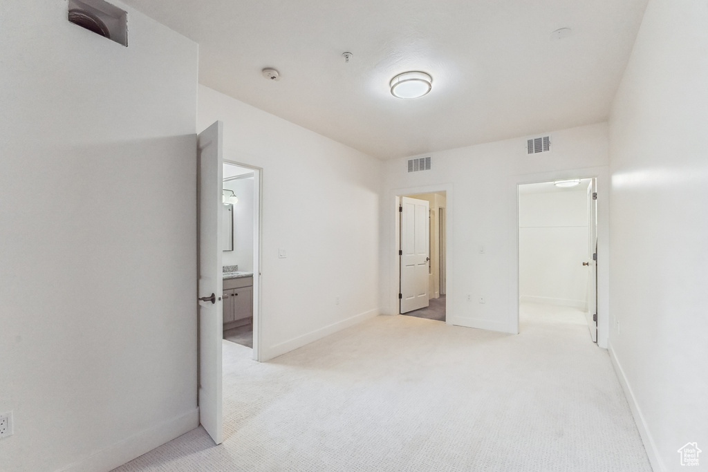 Unfurnished bedroom featuring light colored carpet, a spacious closet, baseboards, and ensuite bath