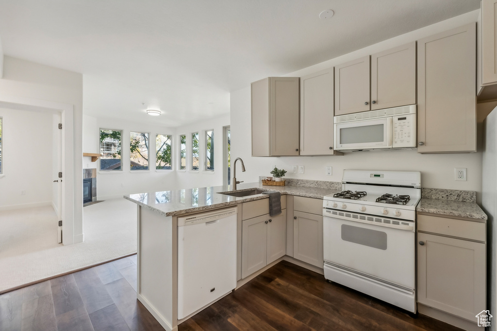 Kitchen featuring white appliances, a sink, dark wood-style floors, a peninsula, and a fireplace with flush hearth