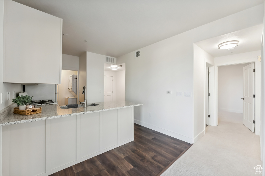 Kitchen featuring a peninsula, a sink, light stone counters, baseboards, and white cabinets