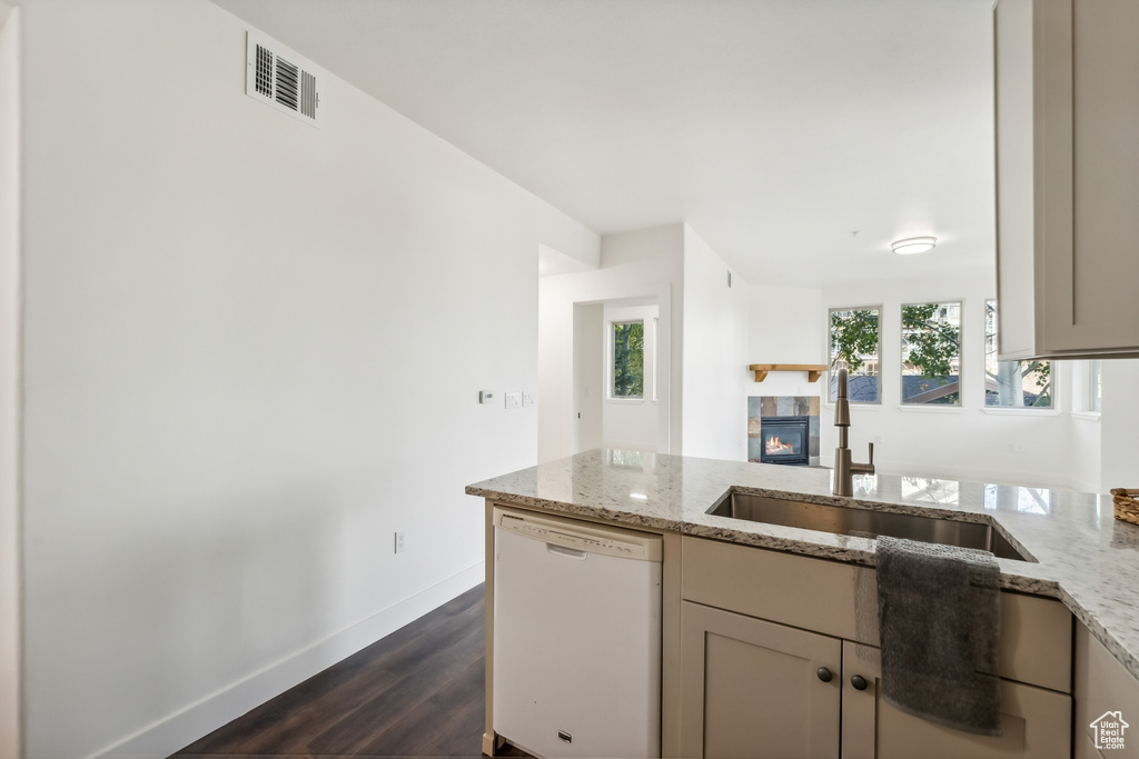 Kitchen with white dishwasher, a sink, a fireplace, light stone counters, and a peninsula