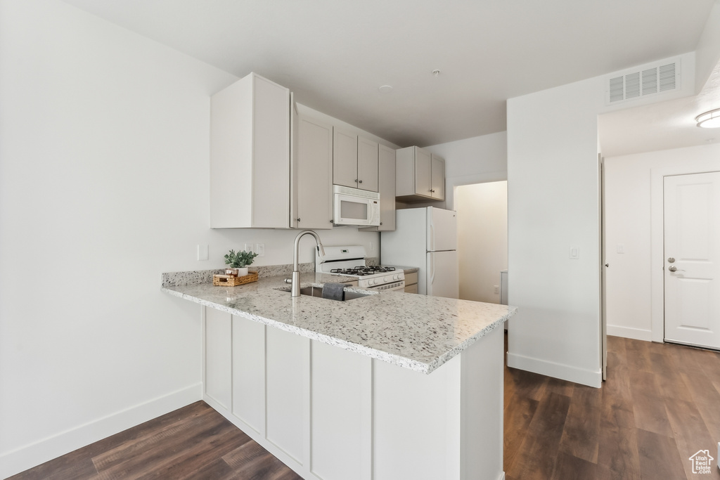 Kitchen with white appliances, a sink, baseboards, dark wood-style flooring, and light stone counters