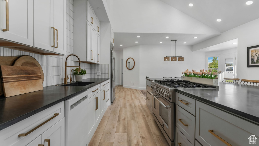 Kitchen featuring premium appliances, a sink, dark countertops, recessed lighting, and light wood-style flooring