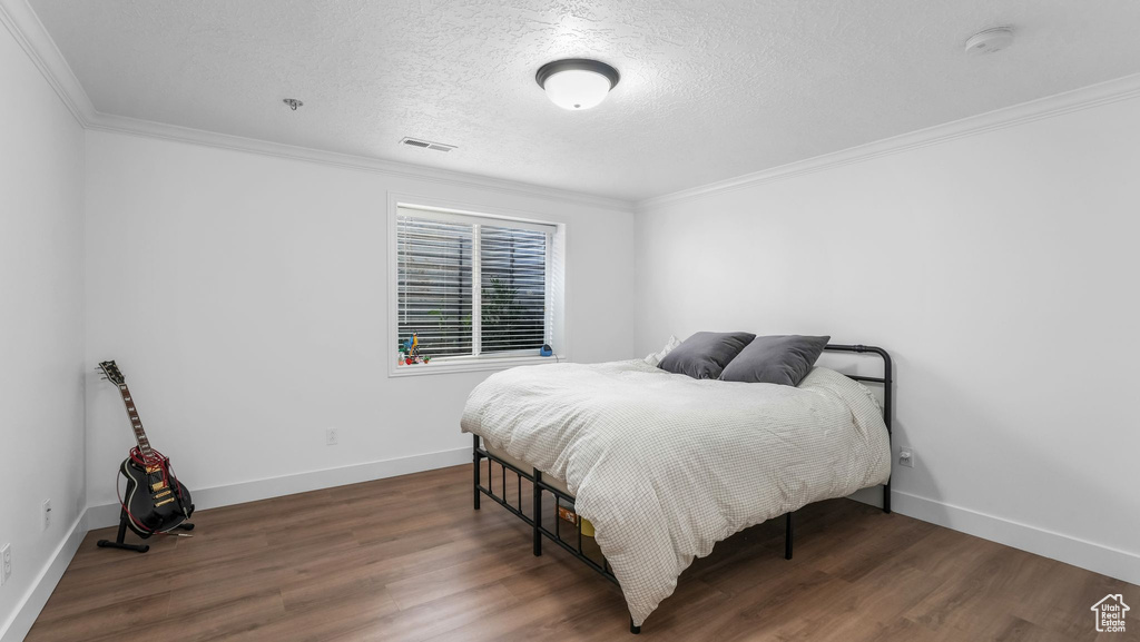 Bedroom with crown molding, wood finished floors, a textured ceiling, and baseboards