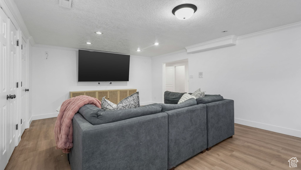 Living area featuring a textured ceiling, baseboards, light wood finished floors, crown molding, and recessed lighting