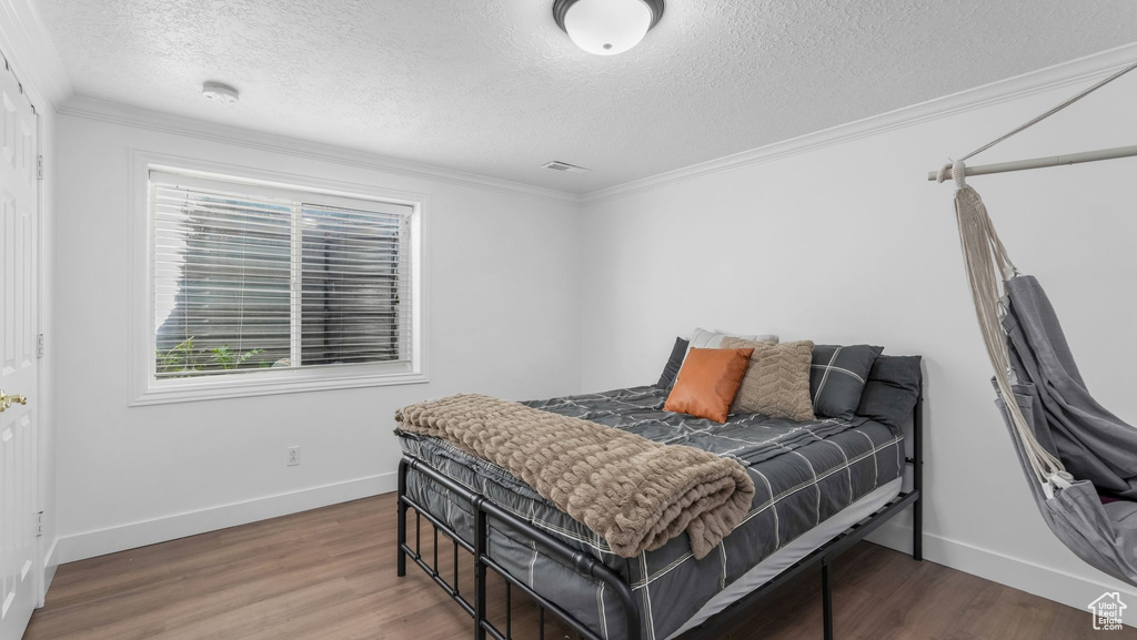 Bedroom featuring a textured ceiling, baseboards, wood finished floors, and crown molding