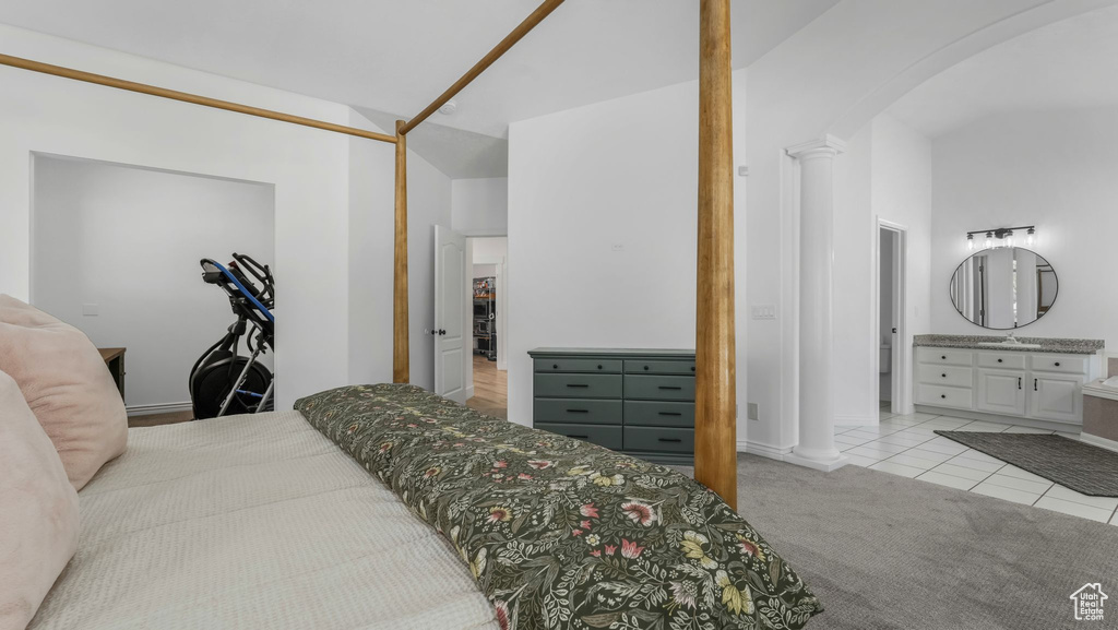 Bedroom featuring arched walkways, ornate columns, light tile patterned floors, light carpet, and a sink