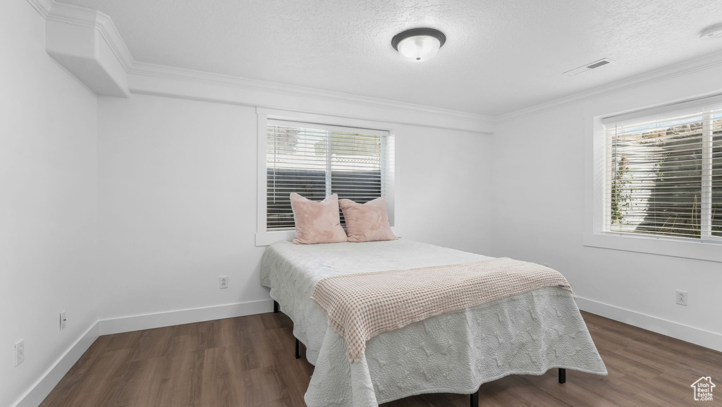 Bedroom with multiple windows, wood finished floors, baseboards, ornamental molding, and a textured ceiling