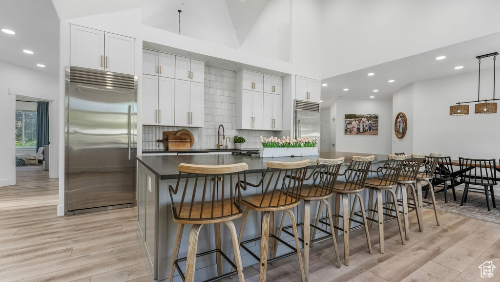 Kitchen featuring built in refrigerator, light wood-style flooring, a spacious island, dark countertops, and white cabinetry