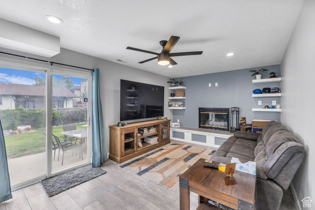 Living area with a glass covered fireplace, a ceiling fan, recessed lighting, and wood finished floors