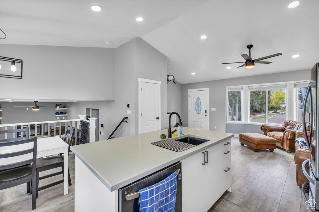 Kitchen featuring a sink, a ceiling fan, dishwashing machine, light wood finished floors, and open floor plan