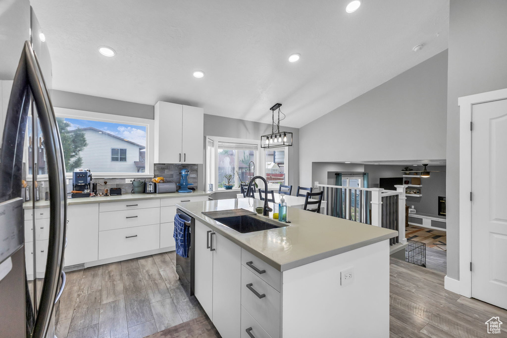 Kitchen with a sink, freestanding refrigerator, lofted ceiling, dishwashing machine, and light countertops