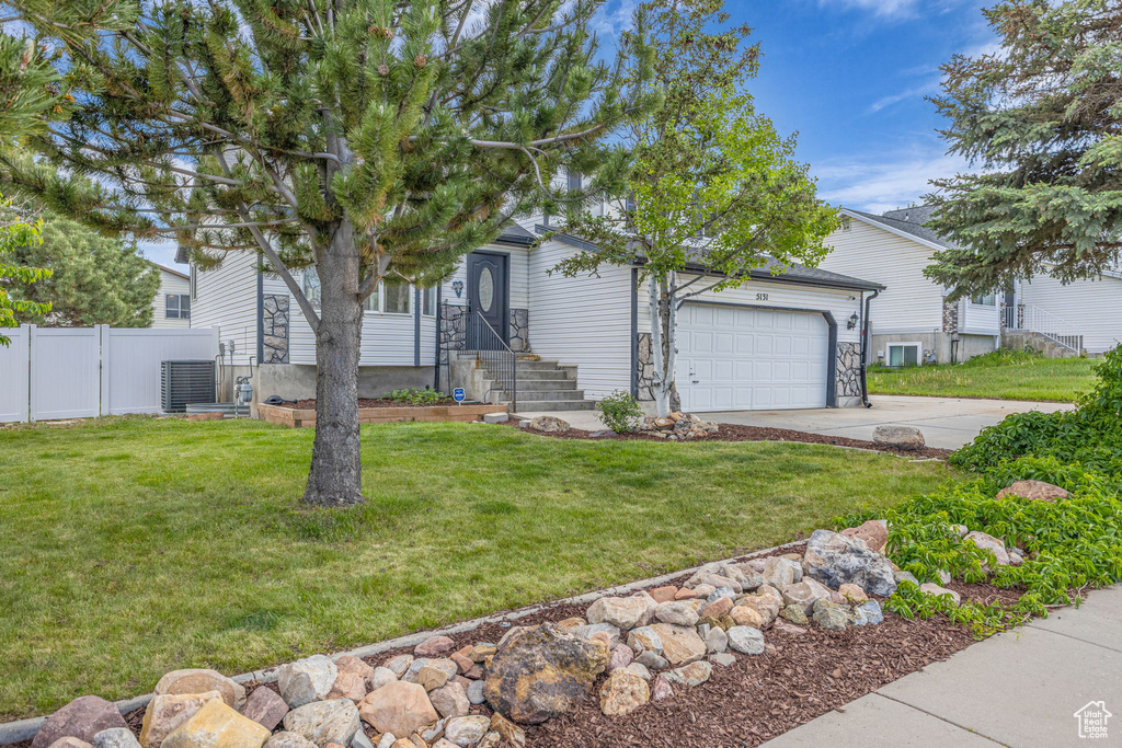 View of property hidden behind natural elements featuring an attached garage, concrete driveway, and central AC