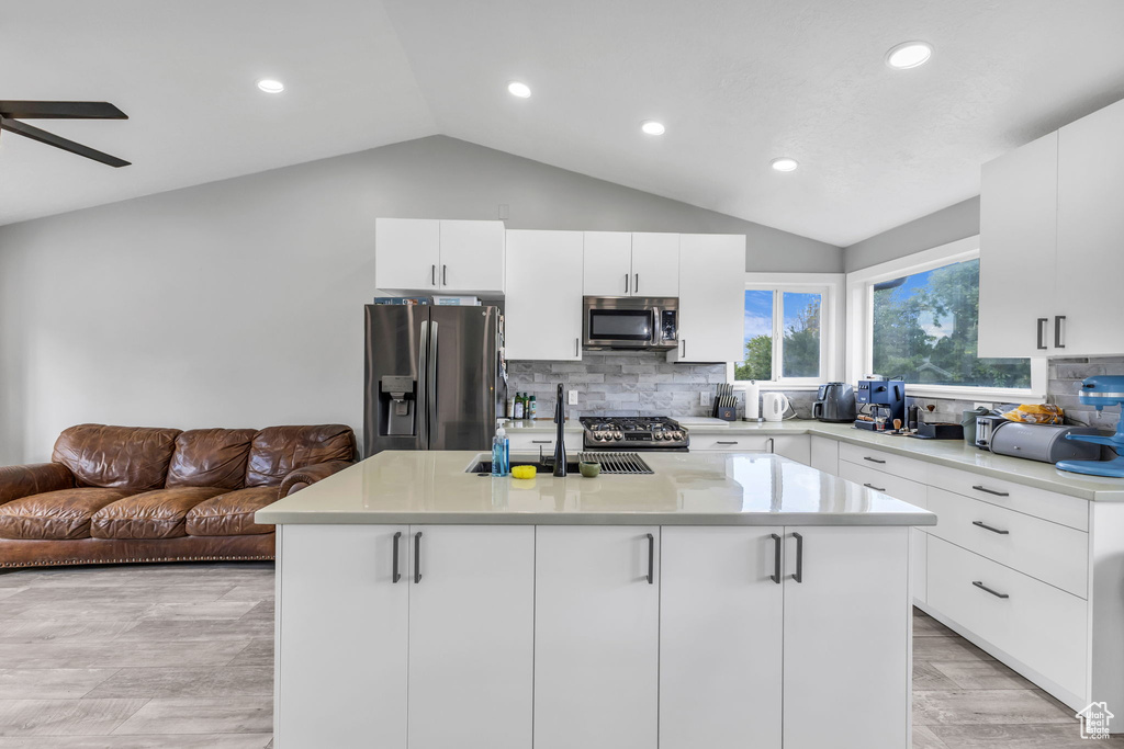 Kitchen with appliances with stainless steel finishes, lofted ceiling, recessed lighting, backsplash, and light countertops