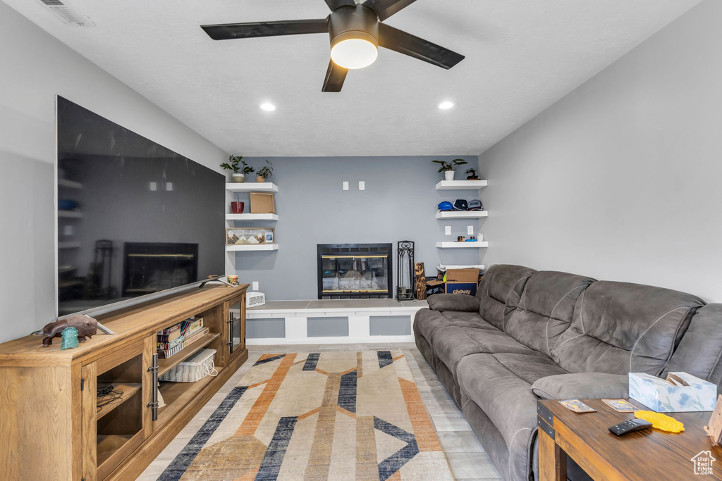 Living area with a glass covered fireplace, recessed lighting, and a ceiling fan
