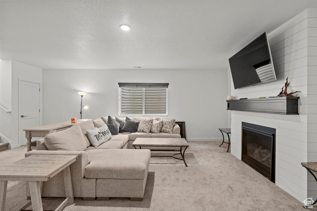 Living area with light colored carpet, a glass covered fireplace, stairway, and baseboards