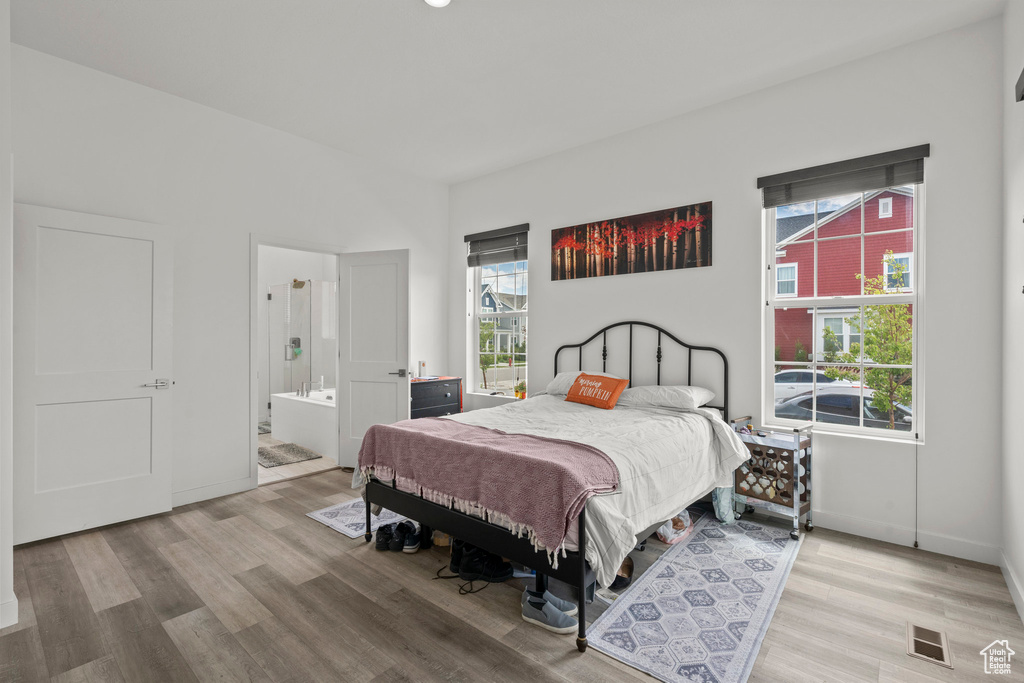 Bedroom with multiple windows, light wood finished floors, ensuite bathroom, and baseboards