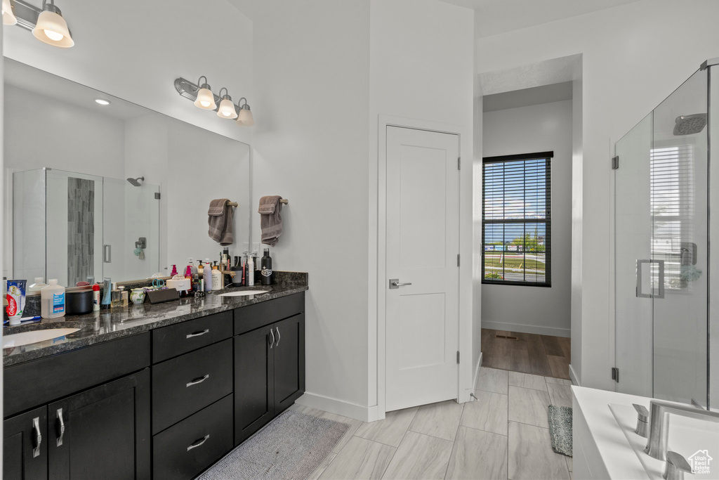 Bathroom featuring a stall shower, double vanity, and baseboards