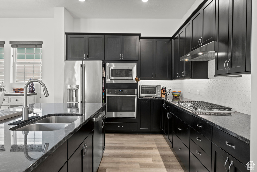 Kitchen with stainless steel appliances, a sink, under cabinet range hood, dark stone counters, and dark cabinets