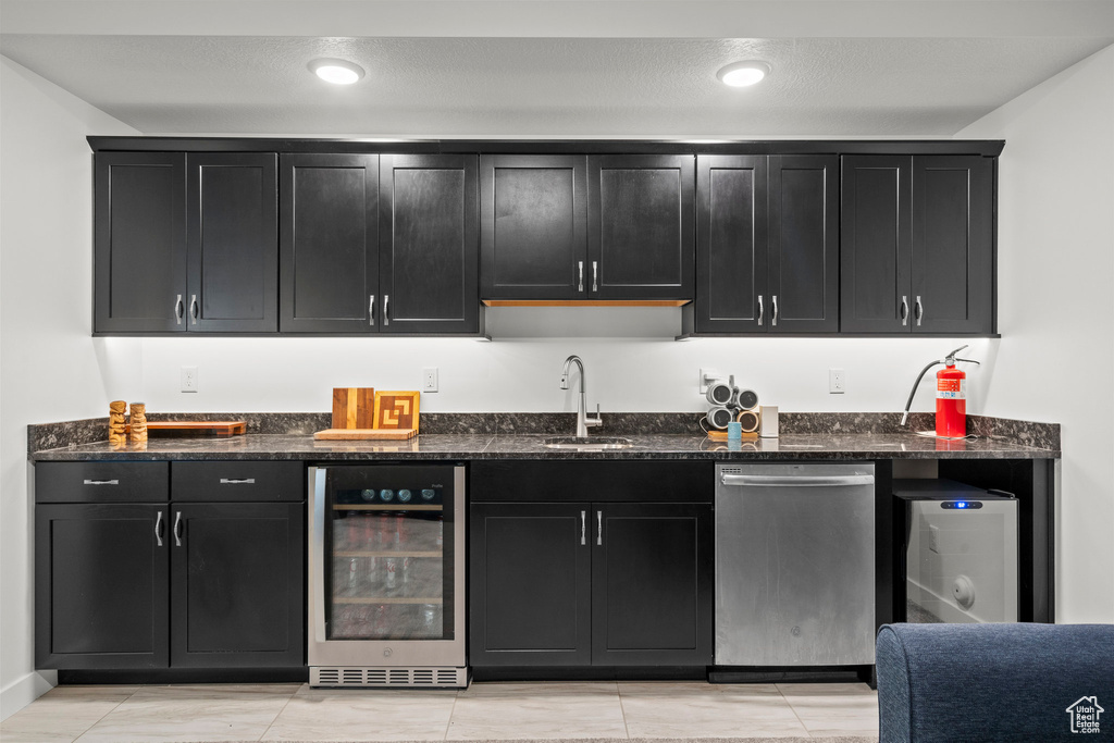 Kitchen with wine cooler, stainless steel dishwasher, dark cabinetry, and dark stone countertops