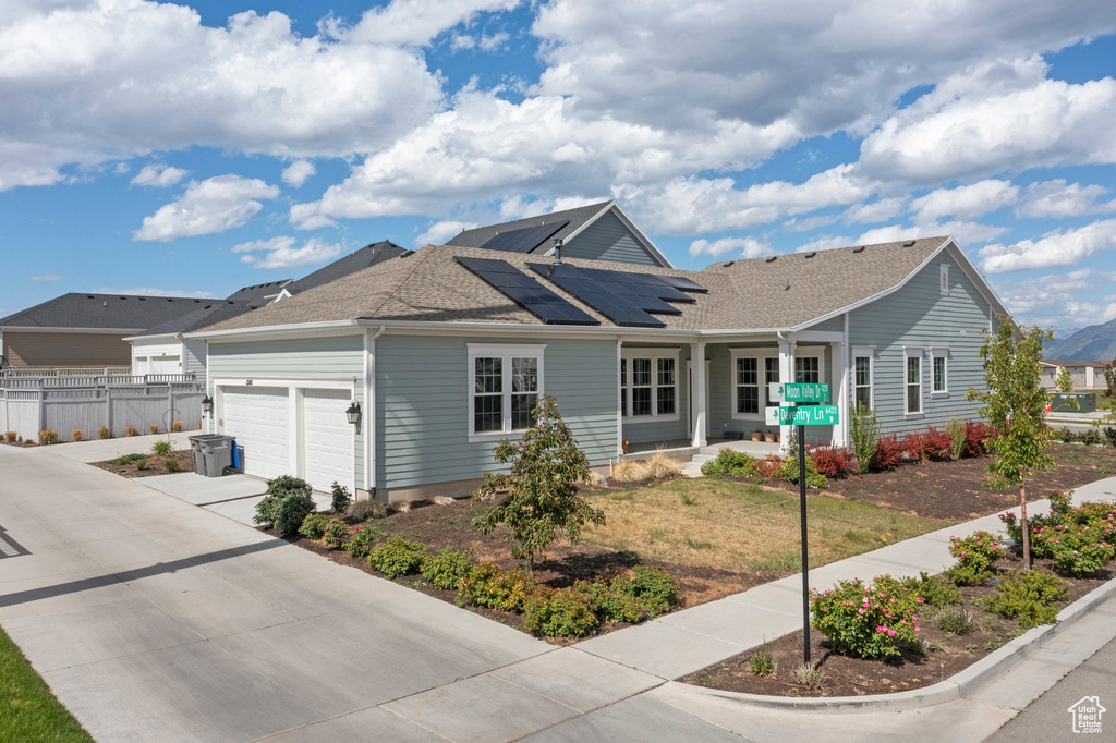Ranch-style home featuring an attached garage, covered porch, solar panels, concrete driveway, and a shingled roof