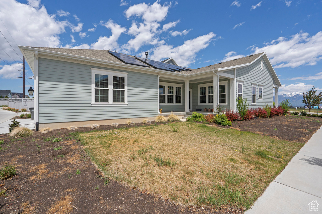 Rear view of house with solar panels, a porch, and a lawn